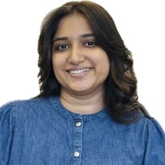 Woman with long dark wavy hair smiling at camera wearing a blue denim button-up shirt